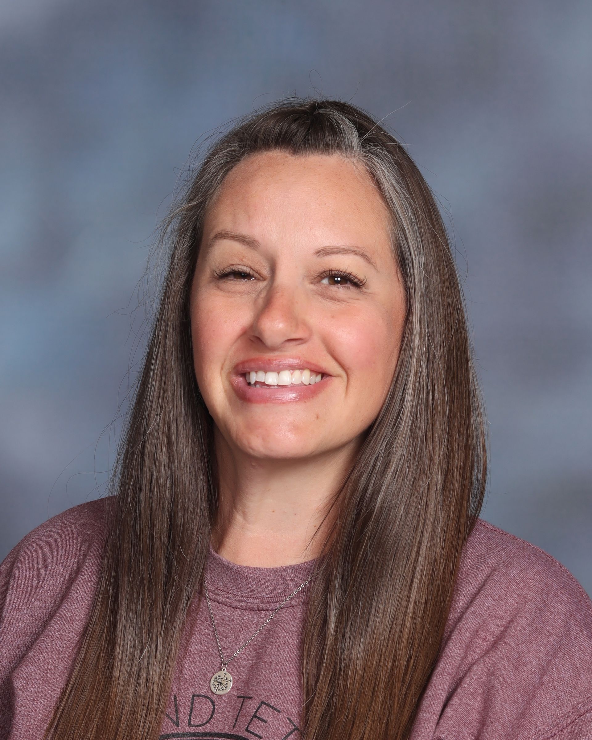 A woman in a purple shirt and earrings is smiling for the camera.