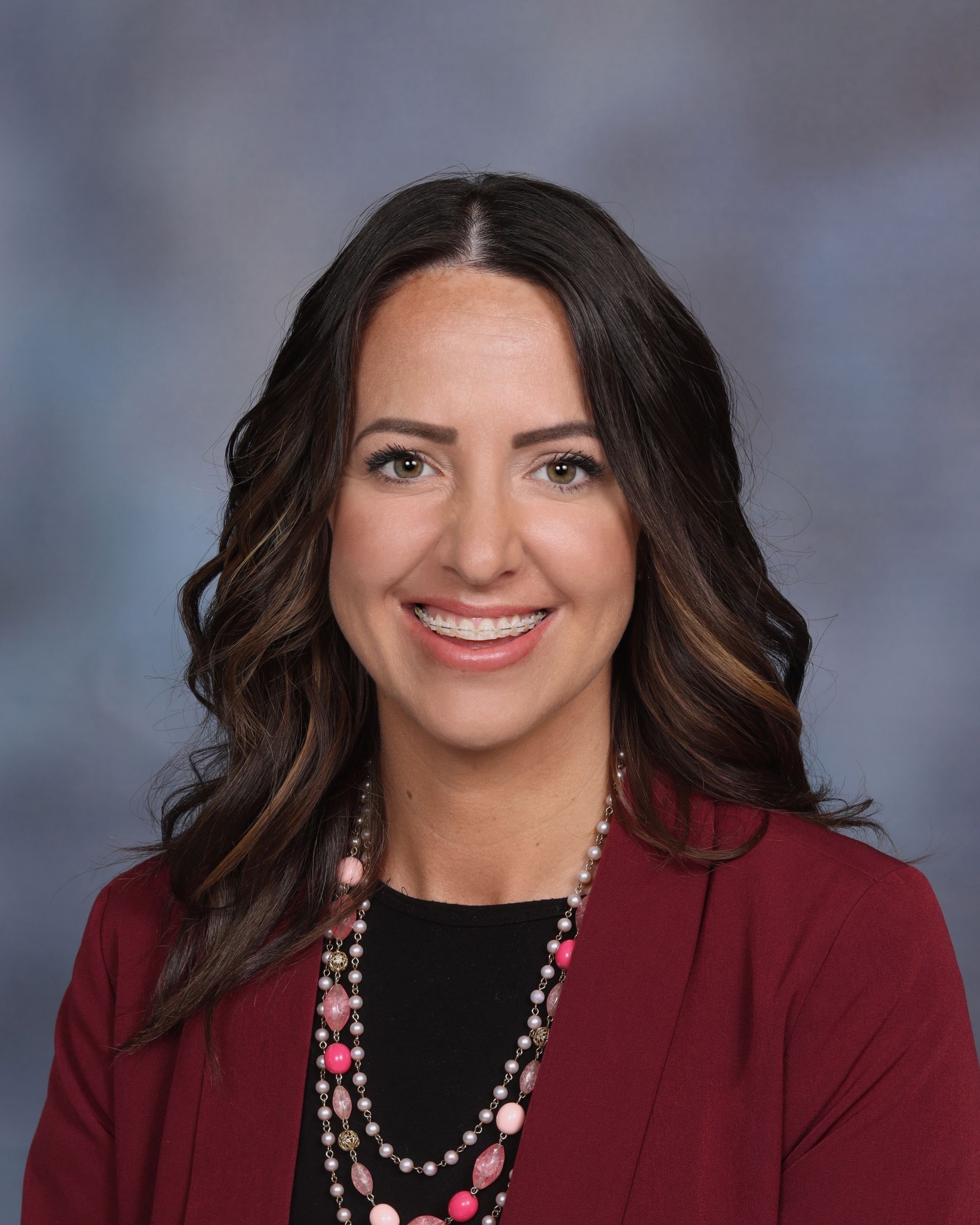 A woman wearing a red jacket and a necklace is smiling for the camera.