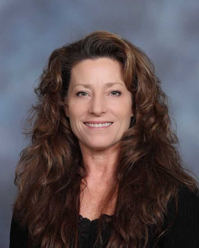 A woman with long brown hair is smiling for the camera.