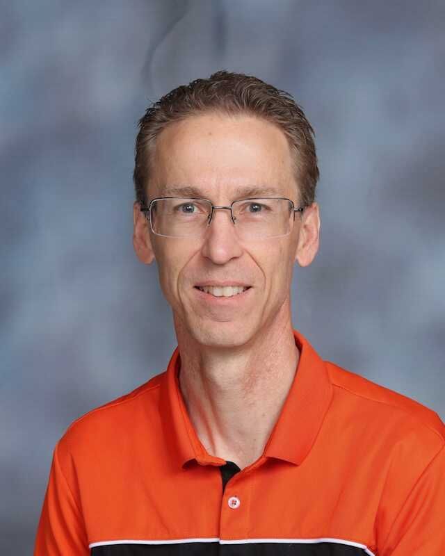 A man wearing glasses and an orange shirt is smiling for the camera.