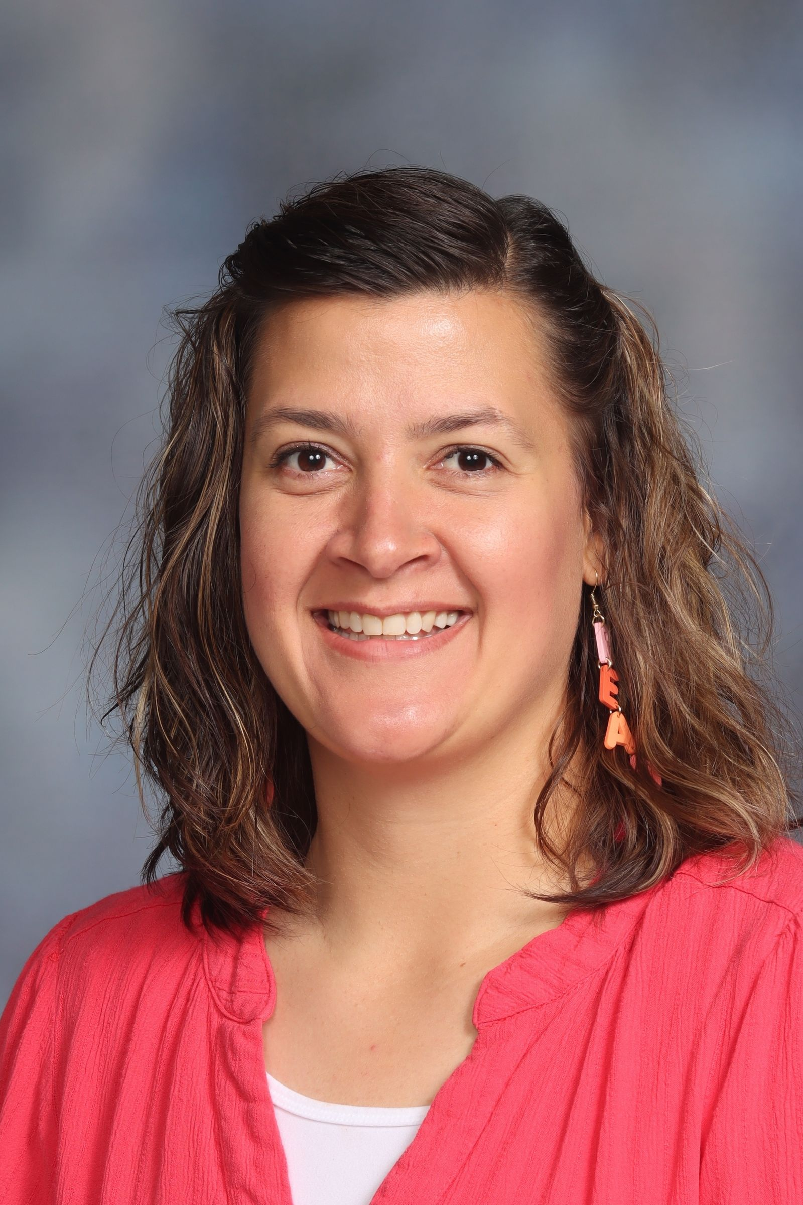 A woman wearing glasses and a pink shirt is smiling for the camera.