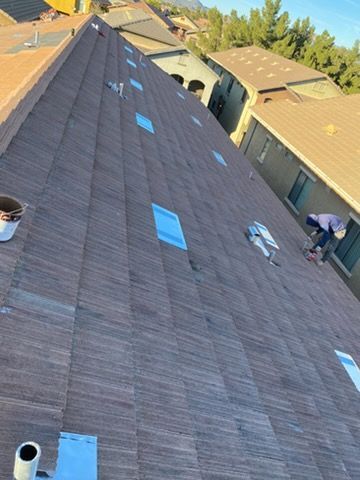 Roofer working on a brown tile roof. Several skylights are visible.