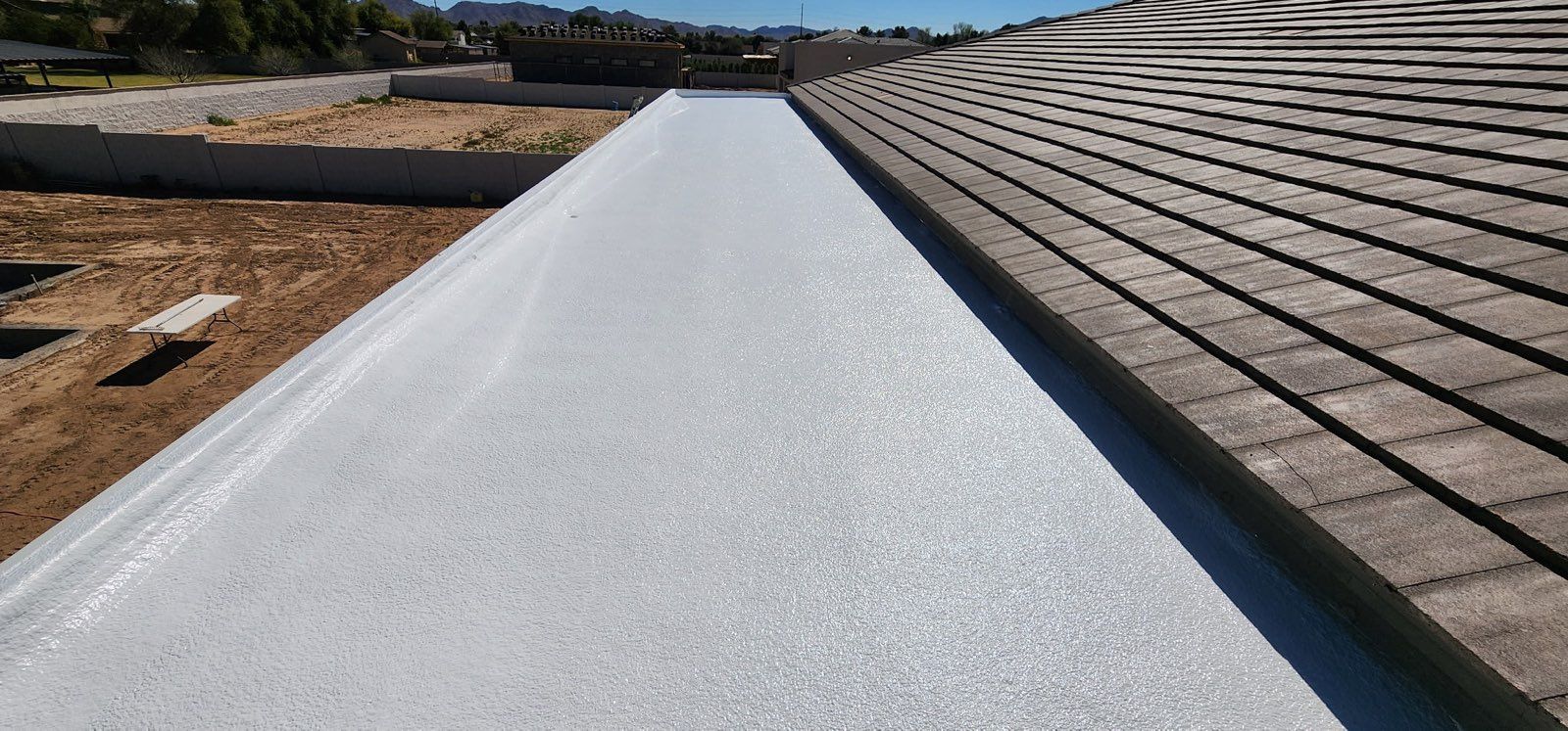 Tan house with brown shingled roof and white trim. Windows with blue sky visible, surrounded by beige siding.