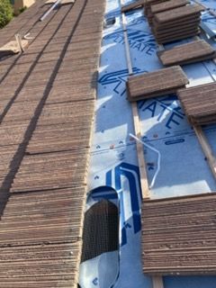 Roof under construction: tiles, blue underlayment, wooden beams, vent opening.