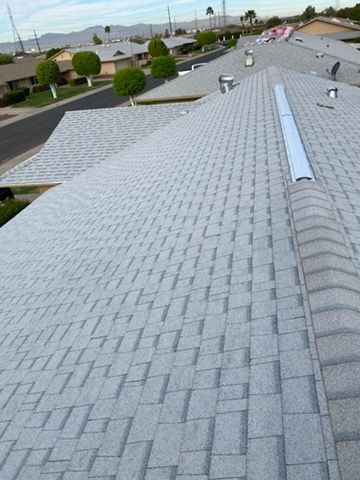 House roof with gray shingles, chimneys, and blue sky with clouds.