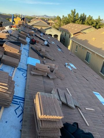 Workers installing roof tiles on a residential house. Tiles are brown, setting is outdoors on a sunny day.
