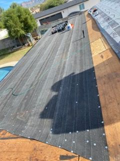 Black roofing underlayment on a house roof, fastened with silver nails; backyard pool in view.