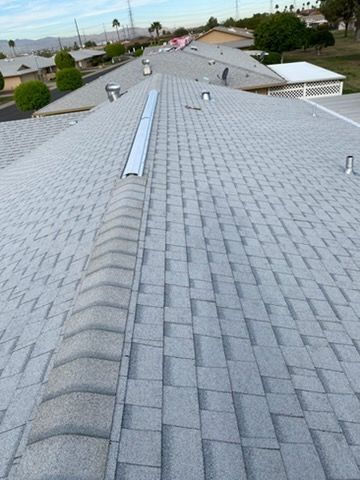 Gray shingled roof with a vent, viewed from above, with other houses in the distance.