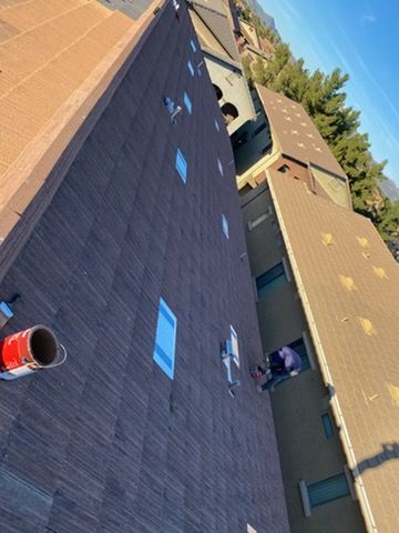 View from above of building with dark brown tiled roof, a person working on the edge, and blue sky.