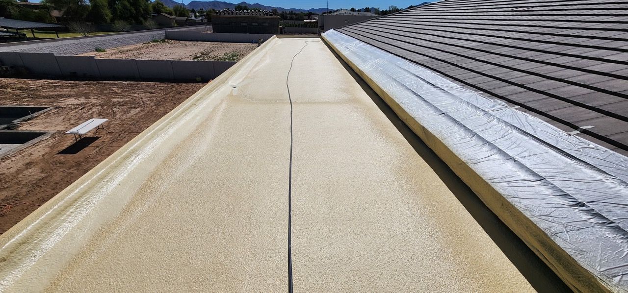 A roof coated in light-colored spray foam, a dark seam running down the center, and a gray roof edge.