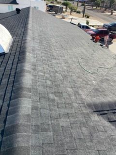 Dark gray shingle roof with a dormer window against a bright blue sky and fluffy clouds.