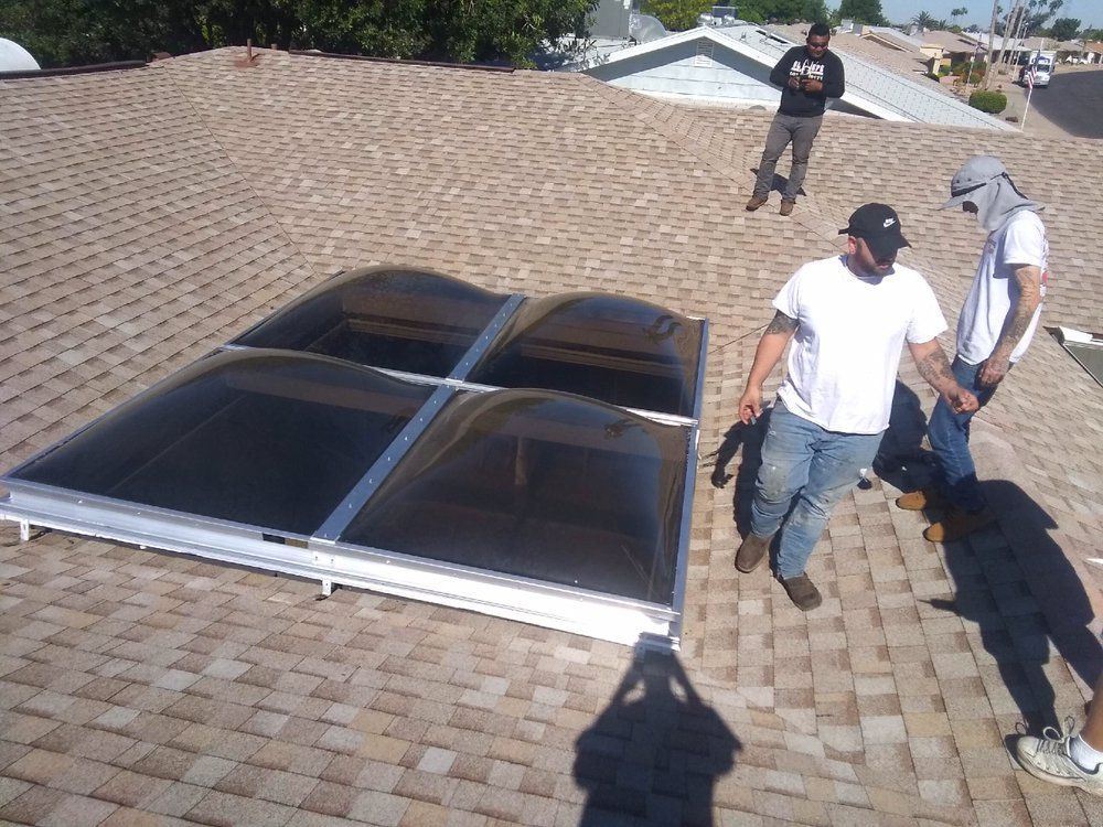 Workers installing a multi-pane skylight on a brown shingle roof. Three men, one dog. Sunny day.