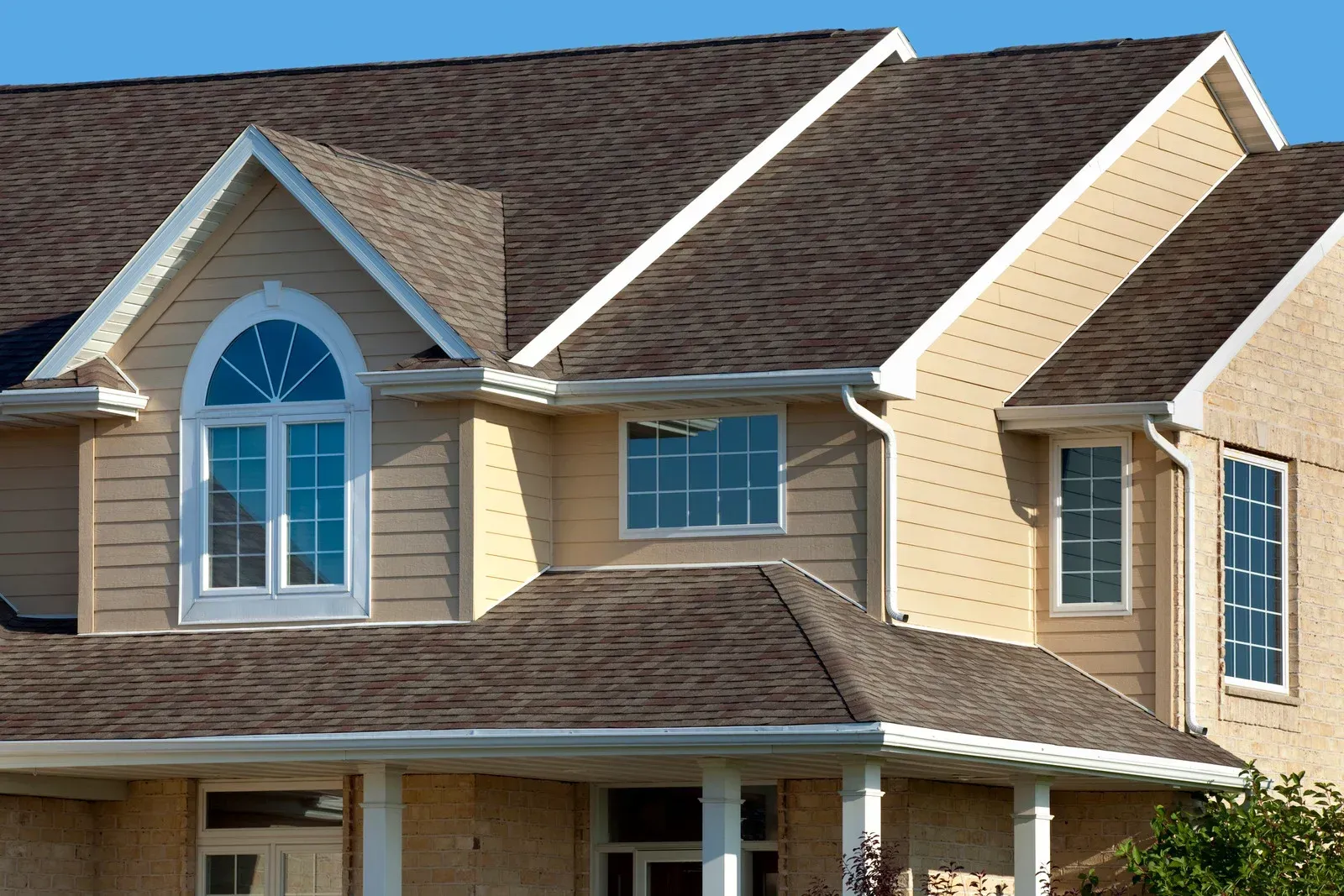 Roofers working on a house roof. One side has shingles, the other has exposed wood.