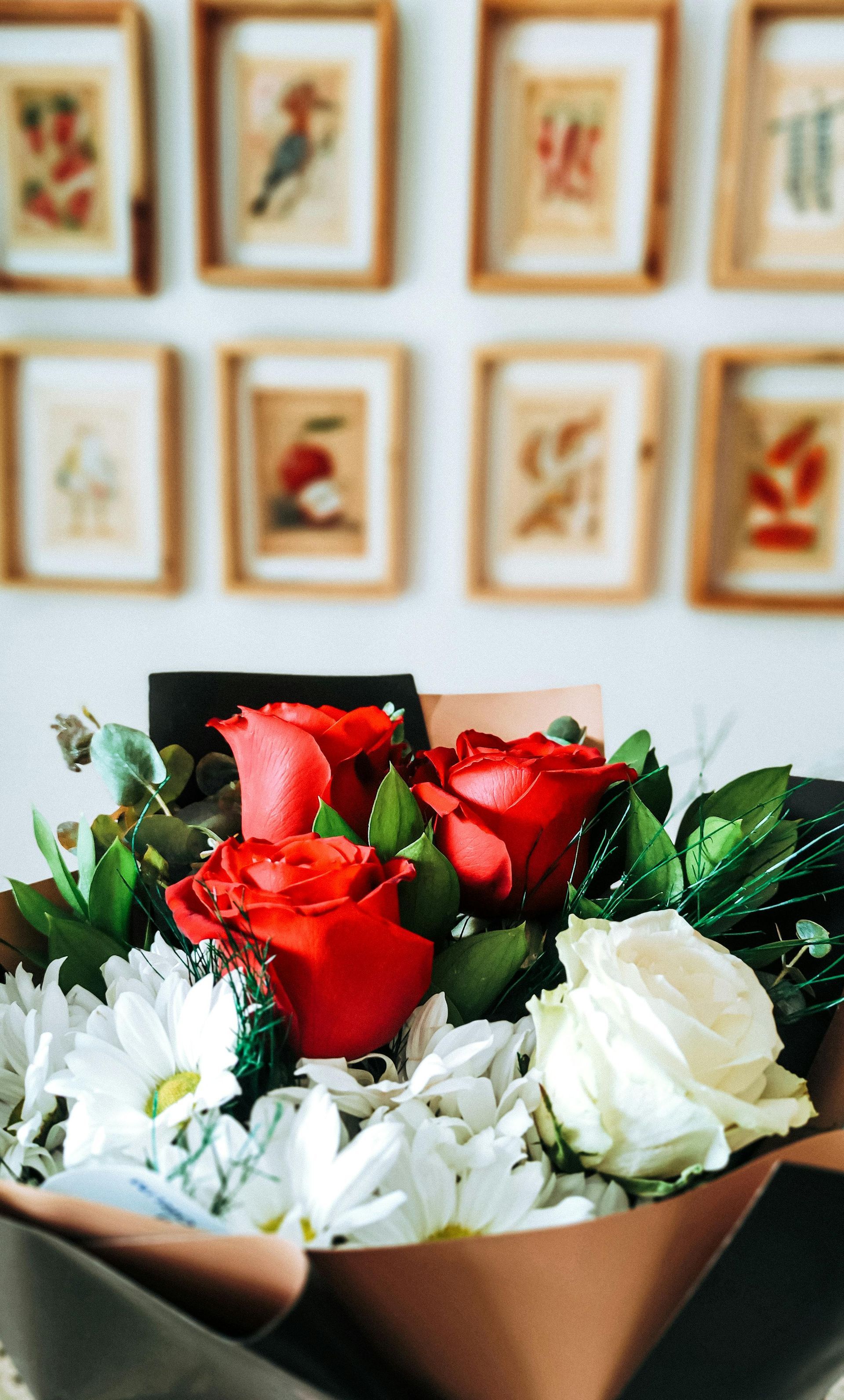 Bouquet de roses rouges et blanches avec feuillage vert, devant un tableau encadré sur un mur blanc.
