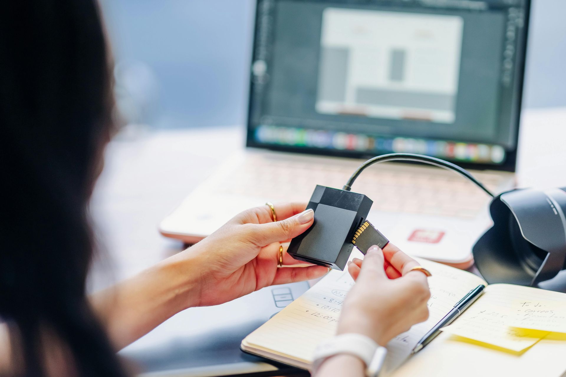 Person inserting a memory card into a black card reader connected to a laptop.