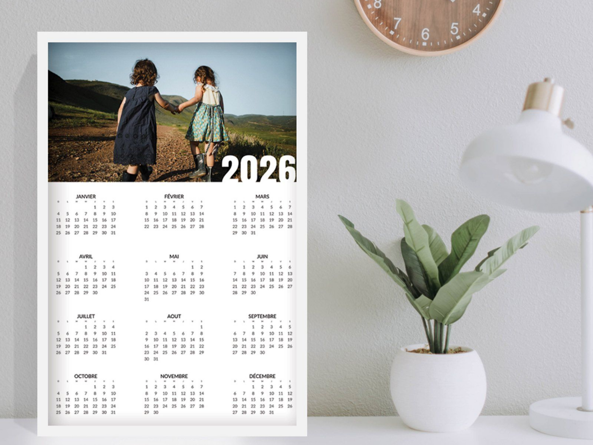 Calendrier 2026 avec la photo de deux personnes se tenant la main. Sur un bureau avec une lampe, une horloge et une plante.
