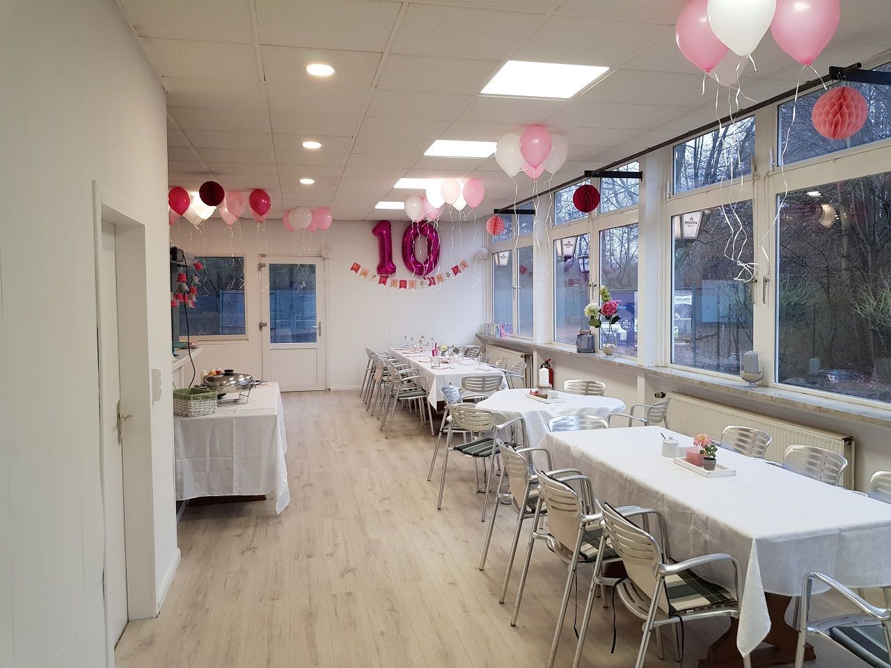 Ein Raum mit Tischen und Stühlen und Luftballons, die von der Decke hängen.