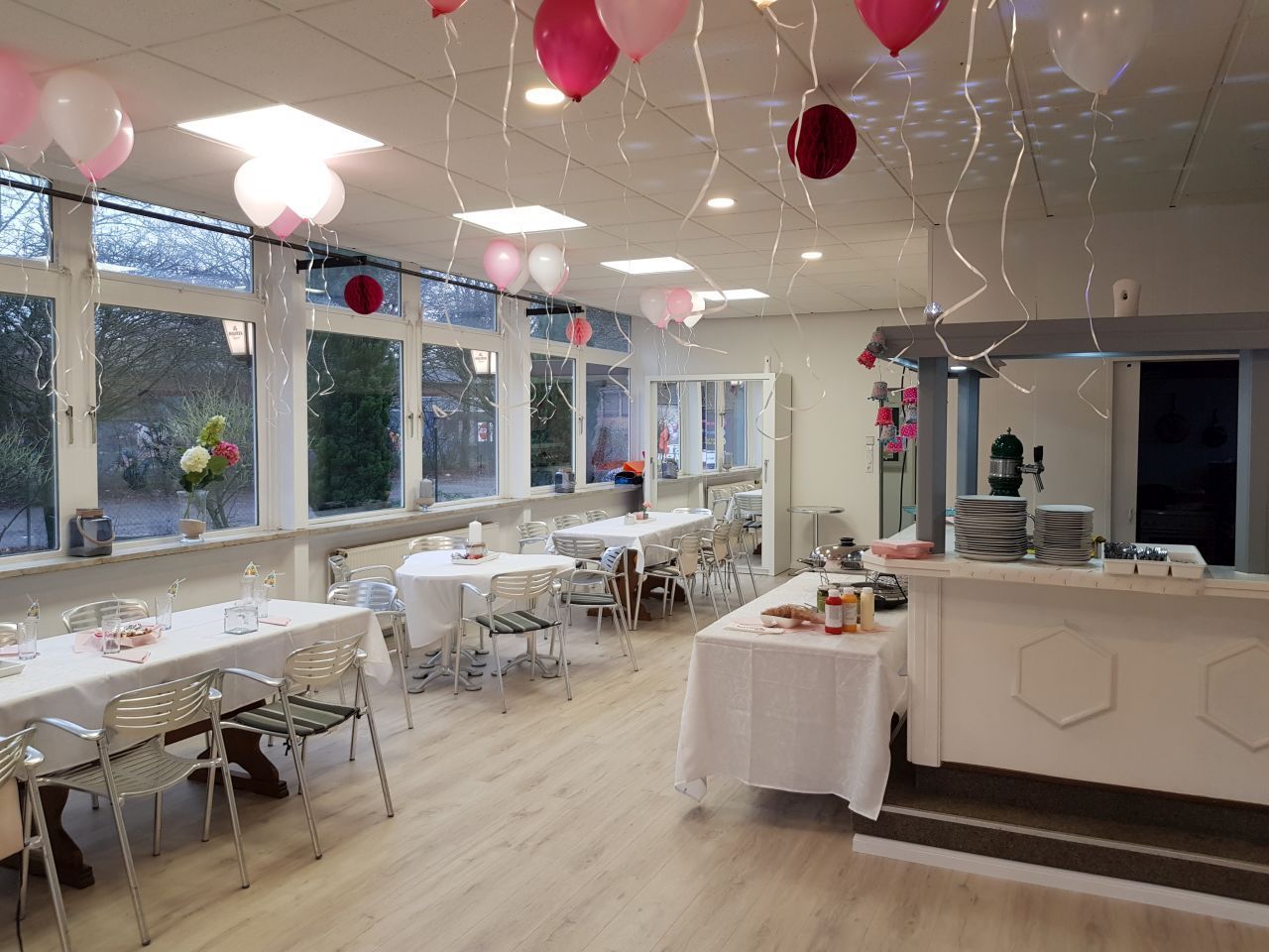 Ein Raum mit Tischen und Stühlen und Luftballons, die von der Decke hängen