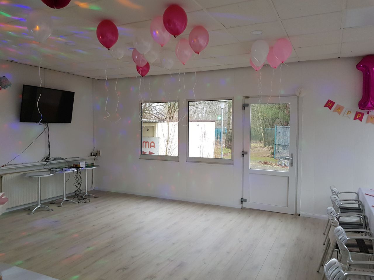 Ein Raum mit von der Decke hängenden Luftballons und Tischen und Stühlen.