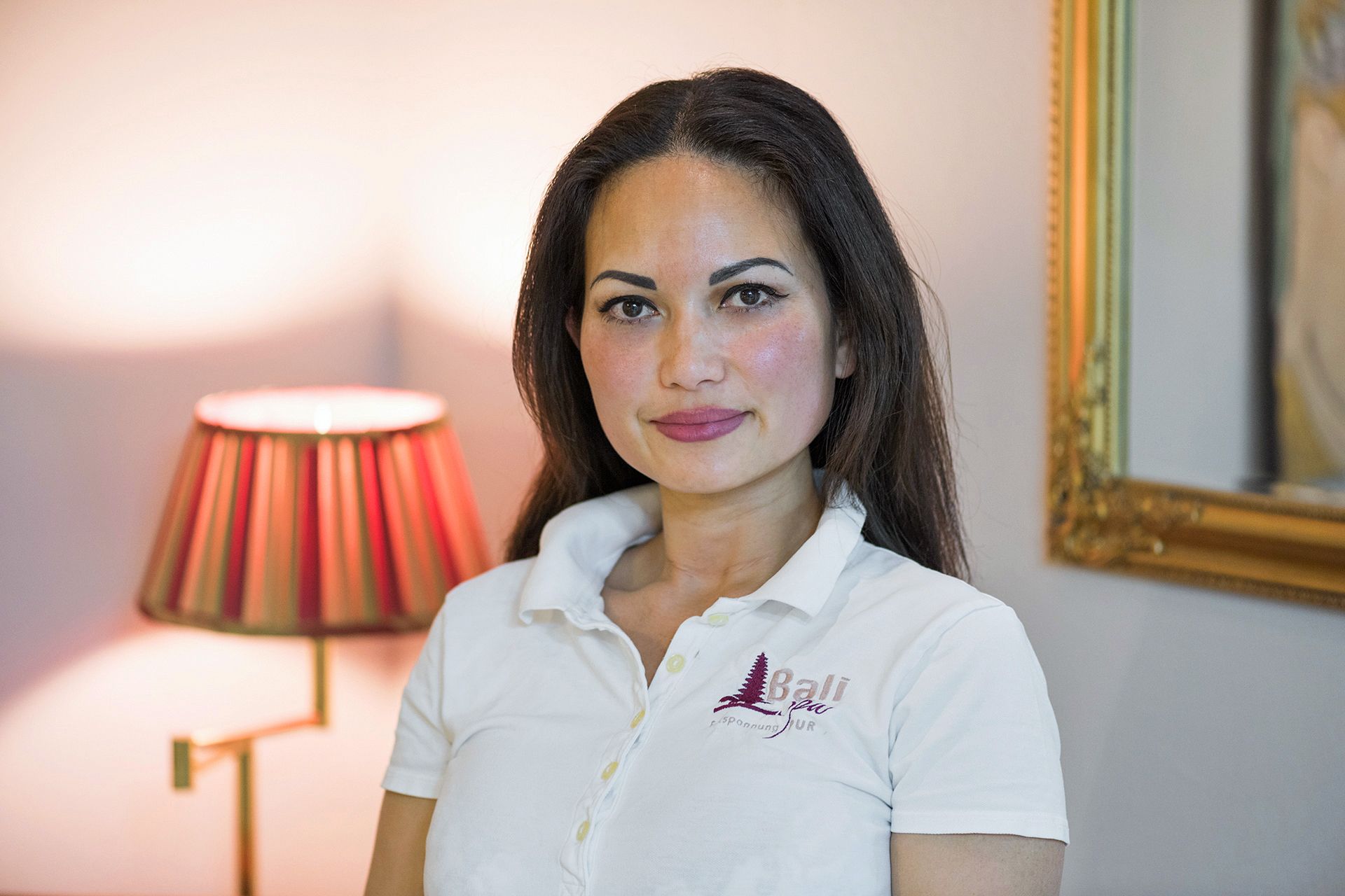 Eine Frau in einem weißen Poloshirt steht vor einer Lampe.