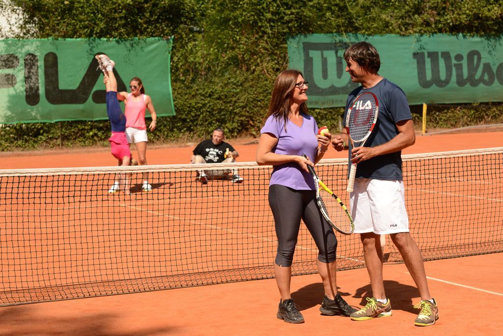 Ein Mann und eine Frau stehen mit Tennisschlägern in den Händen auf einem Tennisplatz.