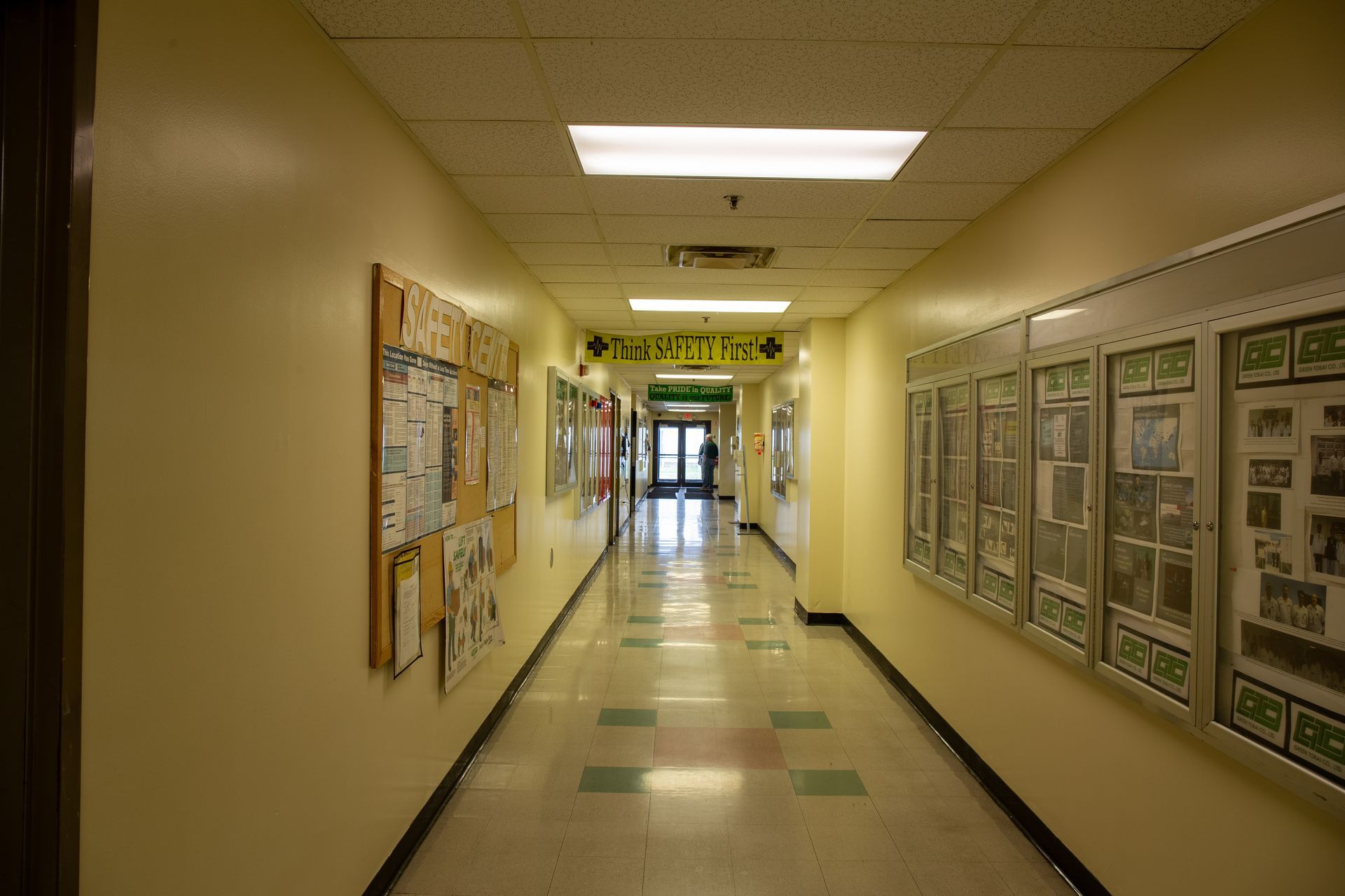 School hallway with bulletin boards, linoleum floor, and bright overhead lights.