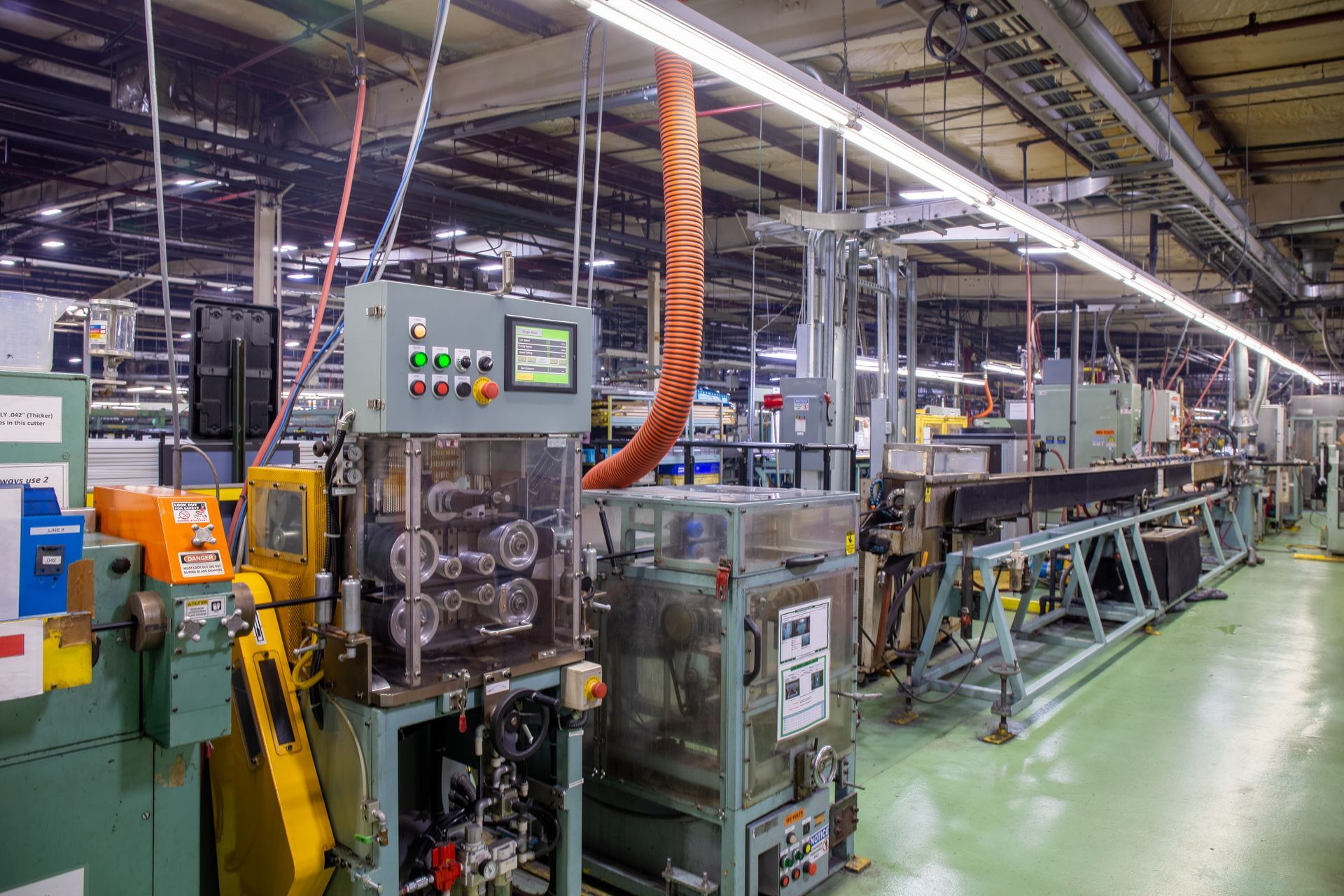 Factory production line with machinery, lights, and cables. Grey and yellow machines.