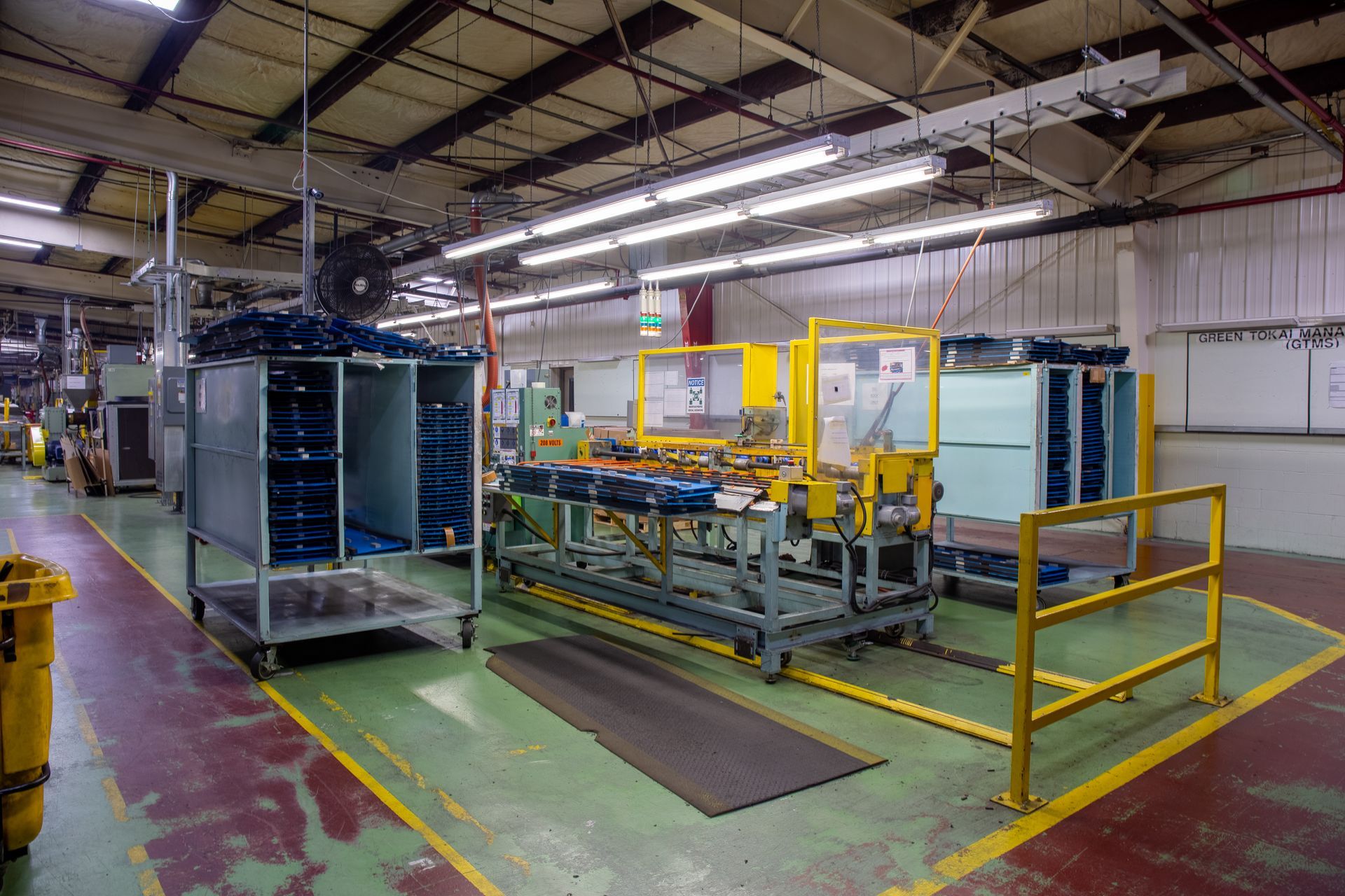 Factory interior with machinery, containers, and a yellow safety rail.