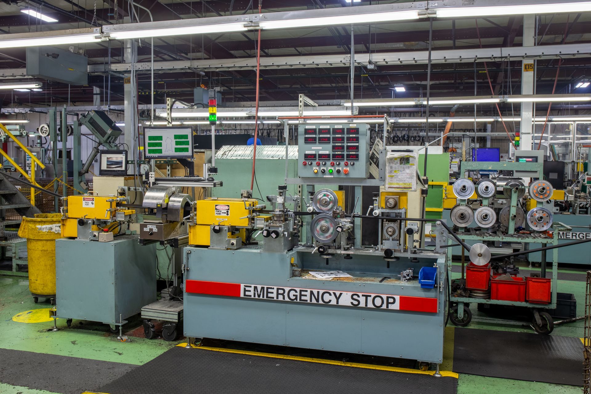 Assembly line machine in factory, with emergency stop button and control panels.
