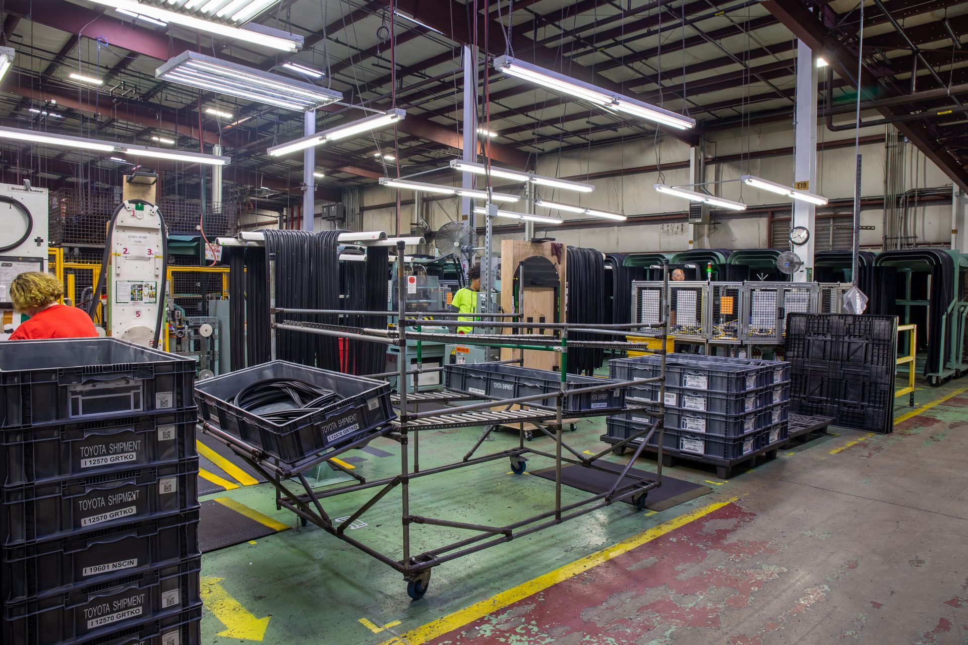 Factory interior with workers near assembly line. Black crates and carts on a factory floor.