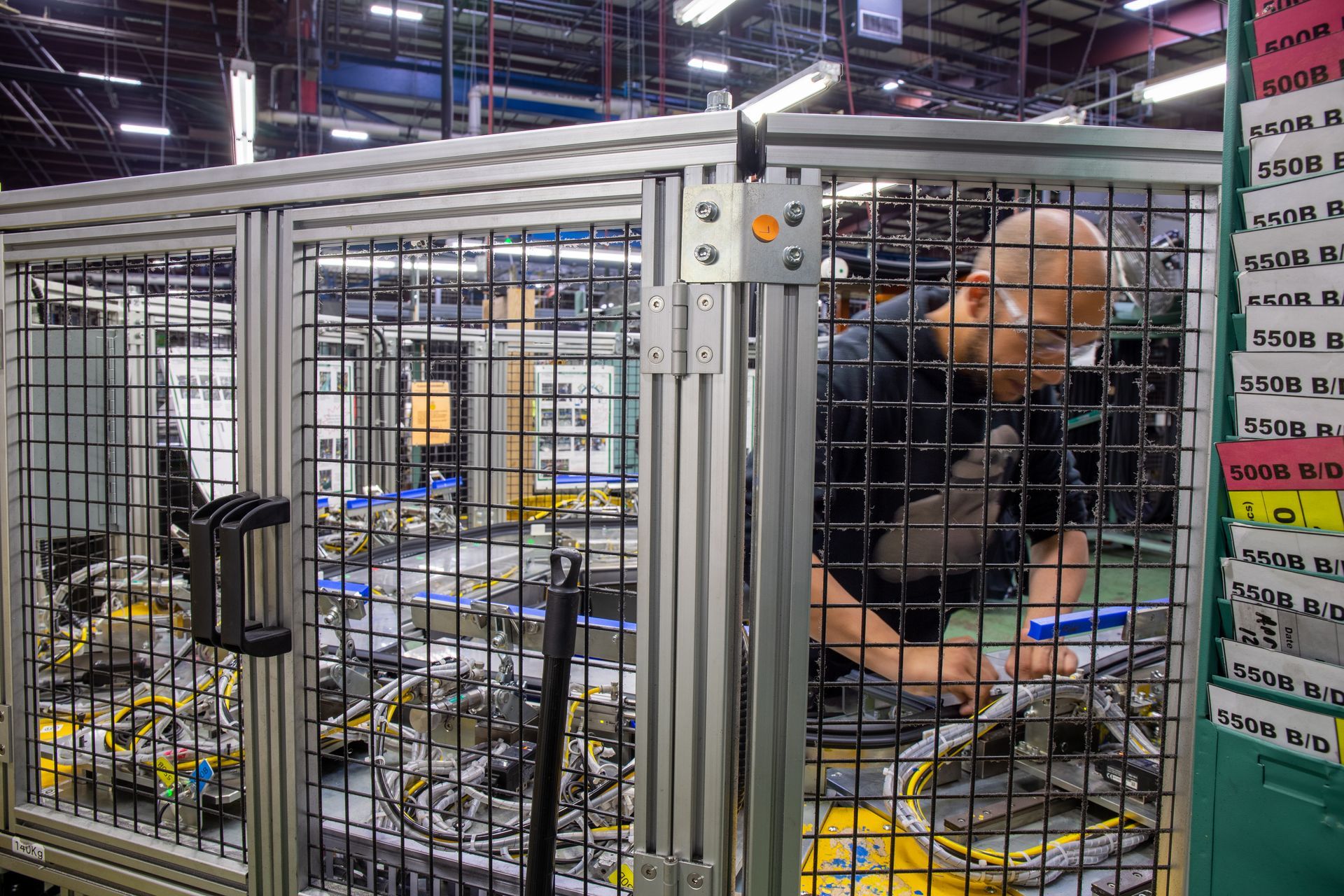 Man working on machinery inside a caged factory station.