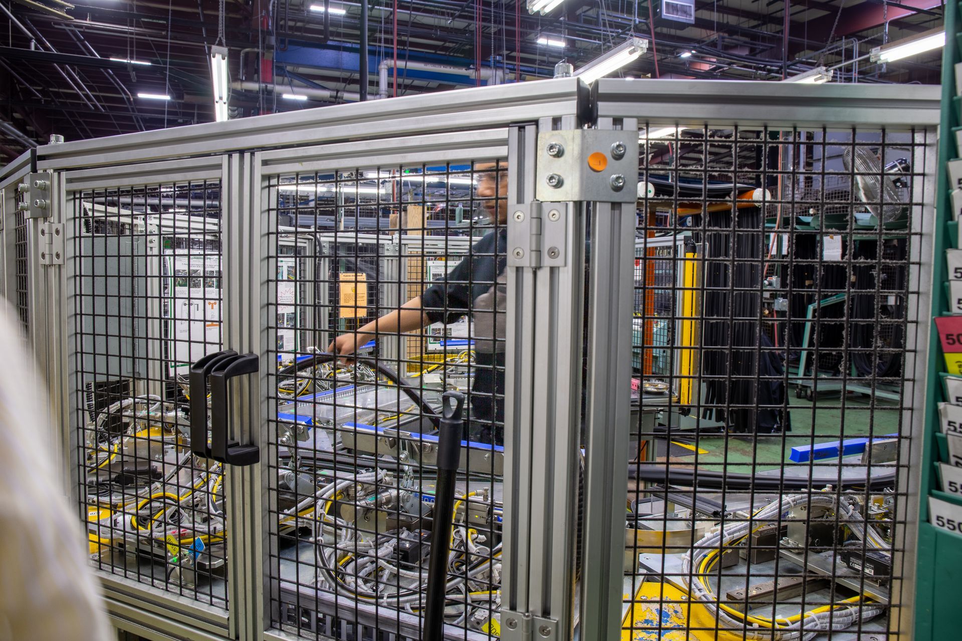 Person working inside a caged industrial machine area, using a hose. Gray metal frame and mesh walls.