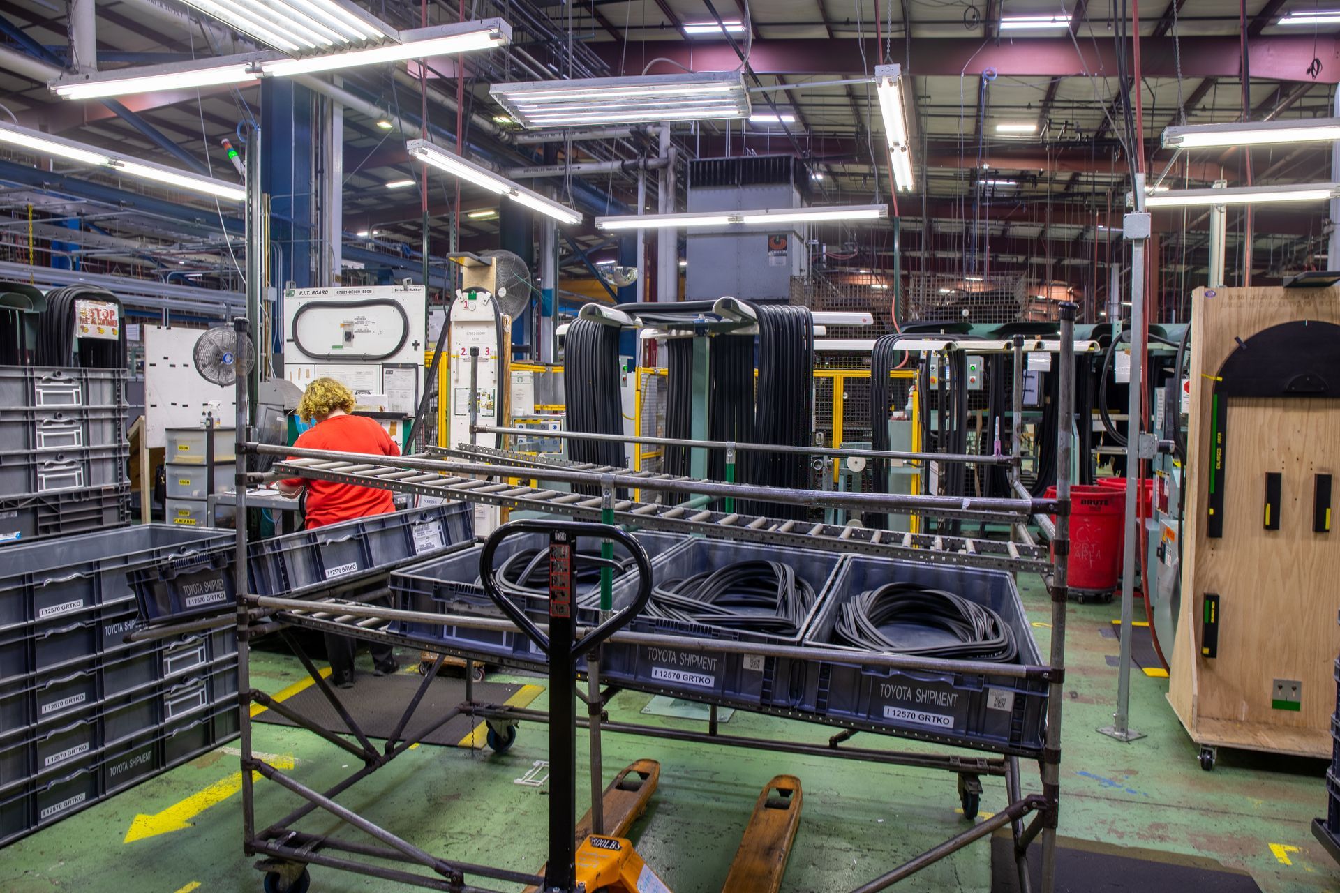 Factory interior with an employee, containers, and a cart loaded with parts.
