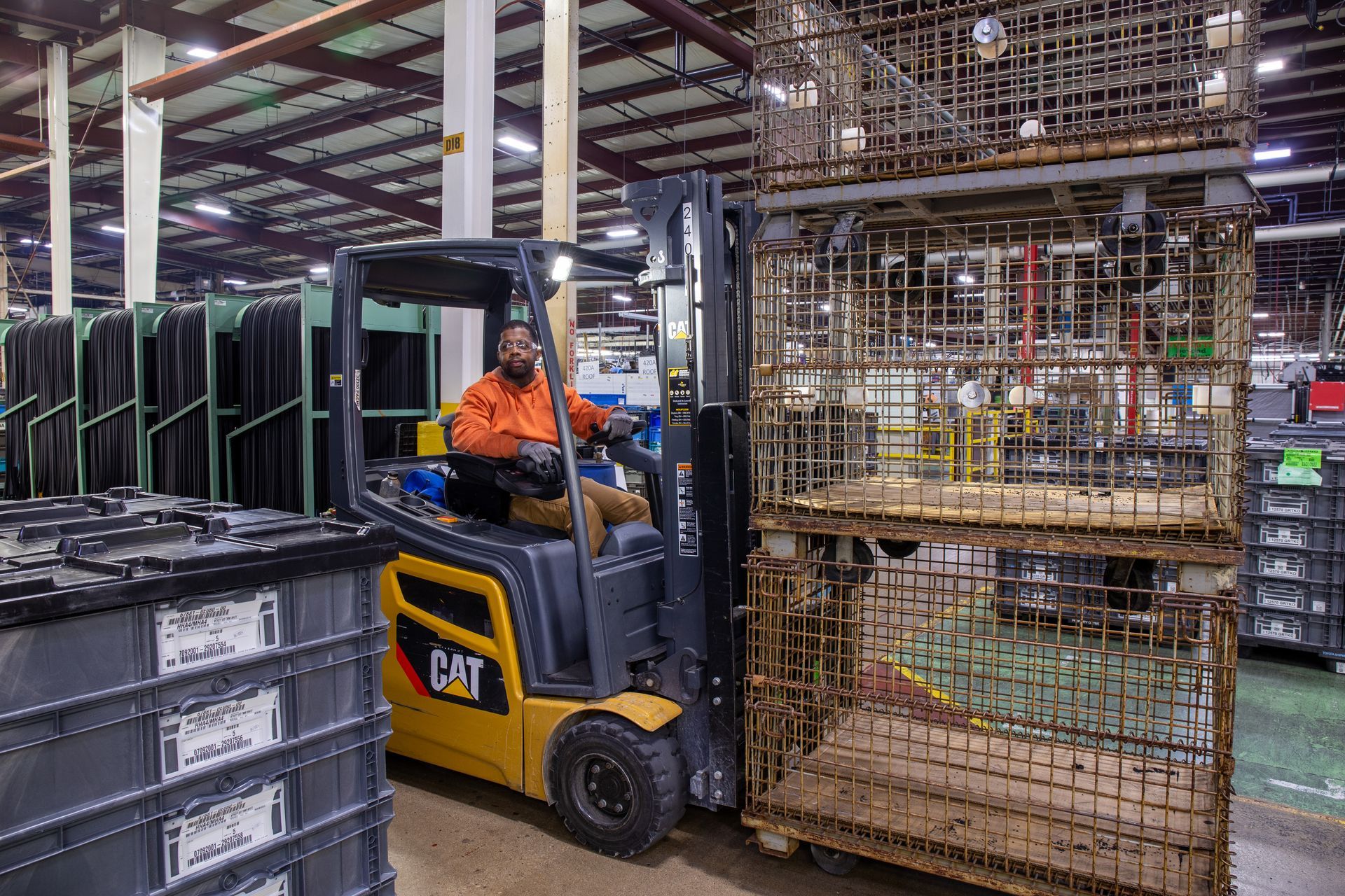 Man operating a yellow forklift in a warehouse, moving stacked metal cages.