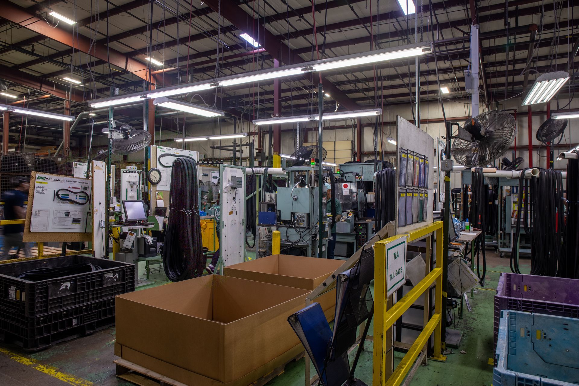 Factory interior with industrial machinery, boxes, and overhead lighting.