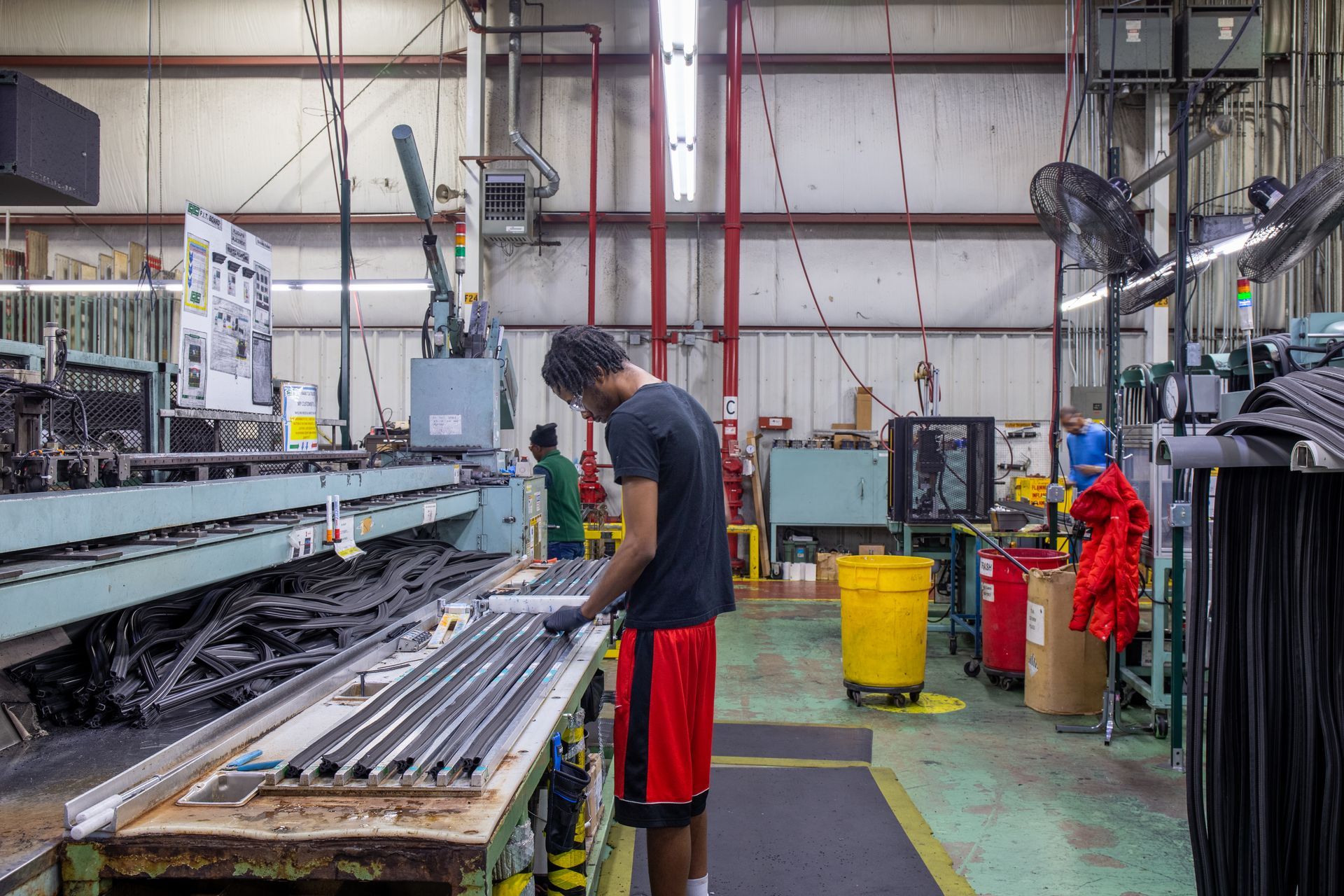Person working on a manufacturing line in a factory. They're wearing a black shirt, red shorts. Factory interior with machinery.