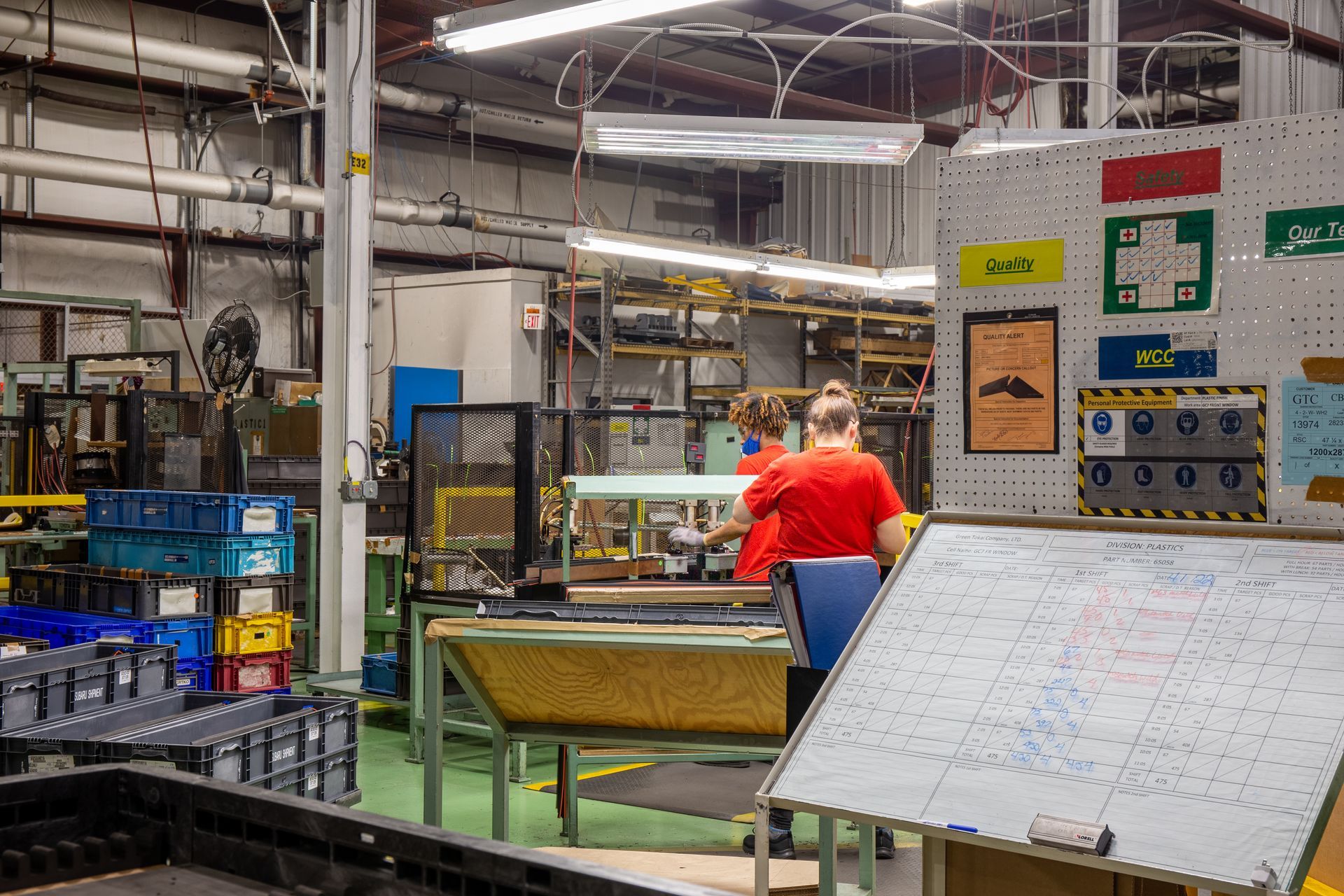 Factory interior with a person in a red shirt working at a machine, and a whiteboard in the foreground.
