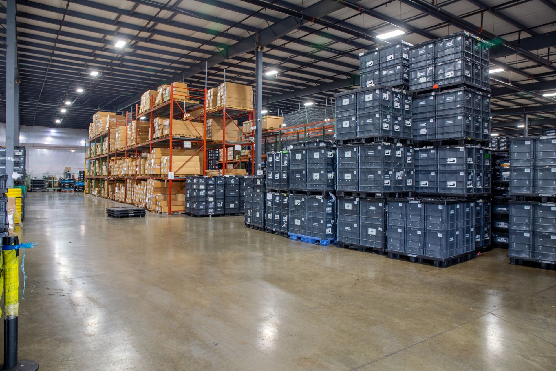 Warehouse interior with stacked boxes and shelving units filled with packaged items.