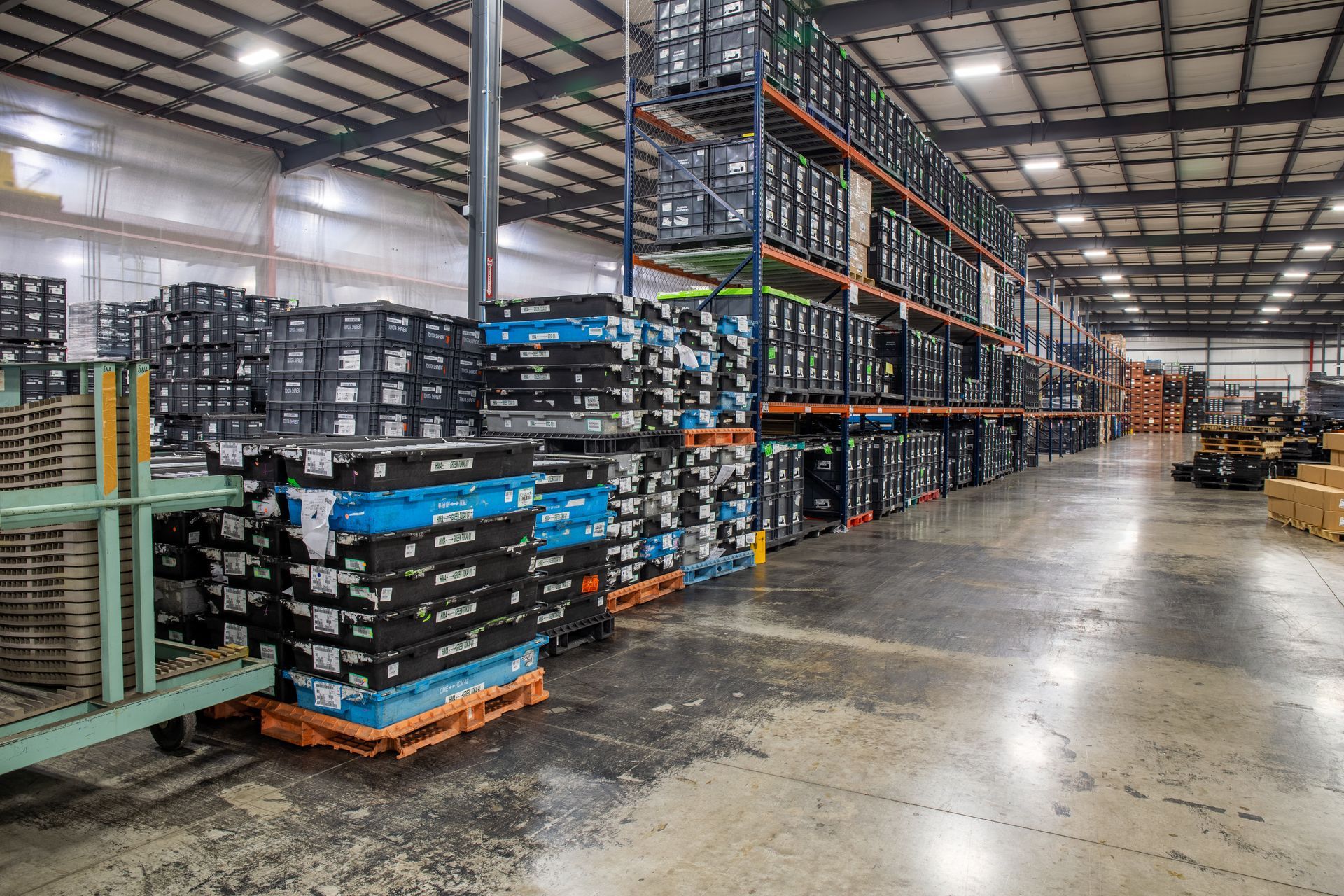 Warehouse interior with rows of storage shelves filled with boxes, and pallets of stacked boxes.