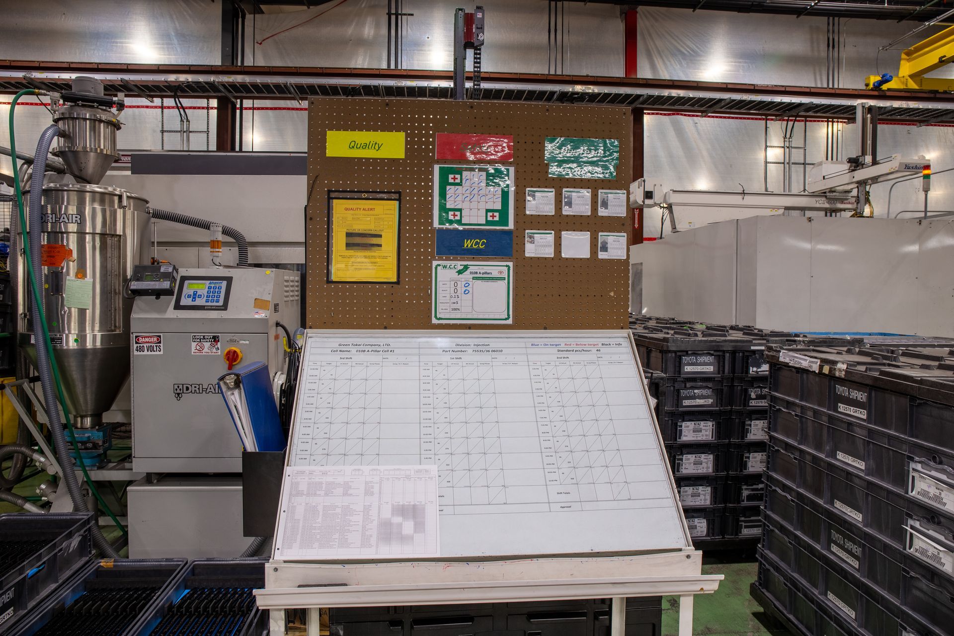 Factory work area with a whiteboard, bulletin board, and machinery.