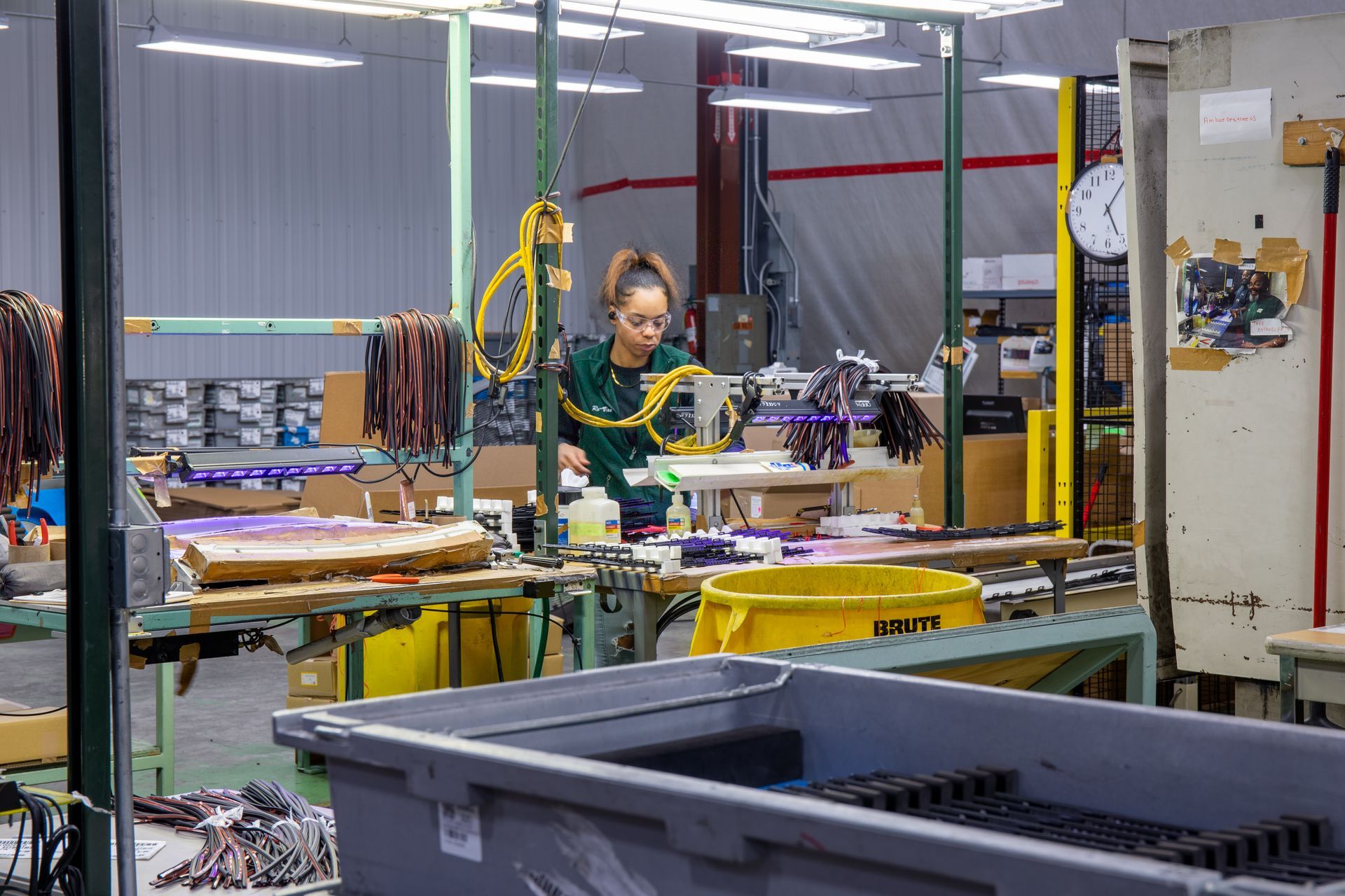 Woman working at a manufacturing station assembling wires, surrounded by equipment and materials.