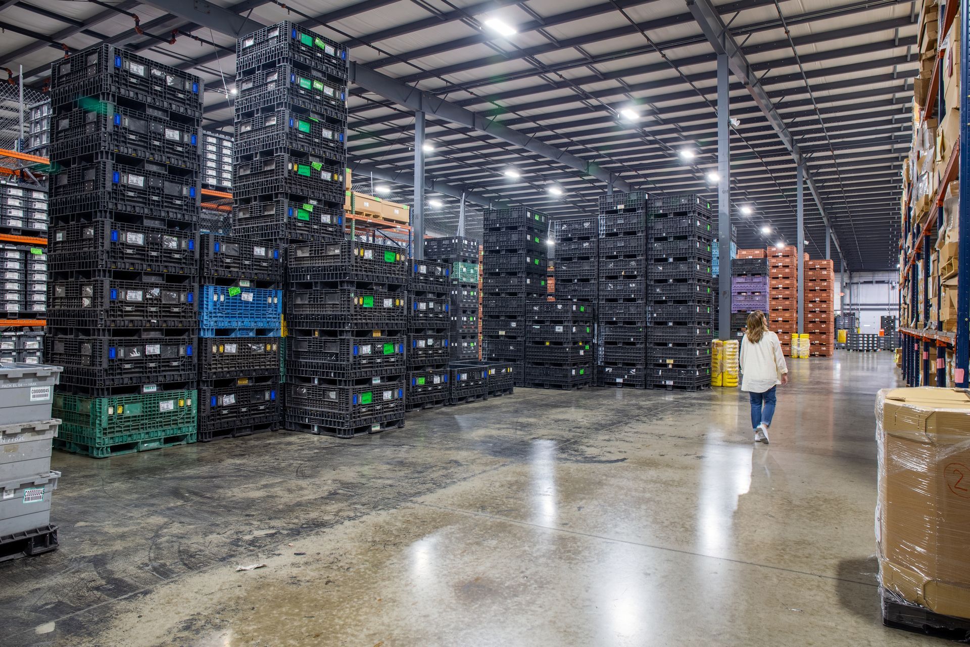Warehouse interior with stacked black bins, racks, and a person walking.