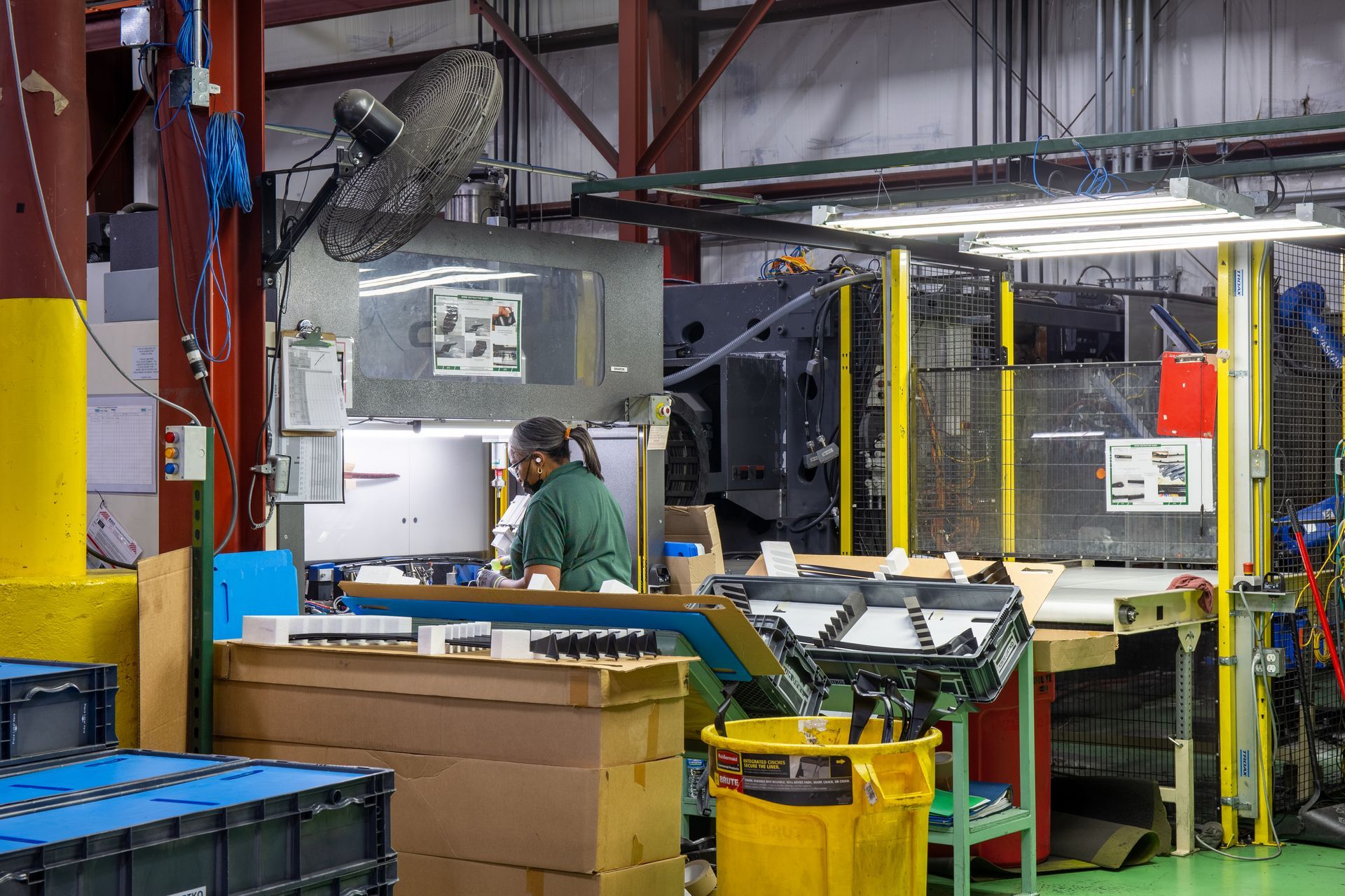 Factory worker at a machine, sorting parts. Industrial setting, metal and plastic components, neutral colors.
