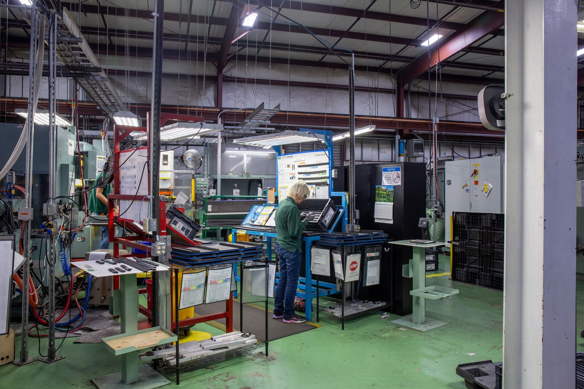 Factory worker operating machinery in an industrial setting. Green floor, metal framework, various equipment.