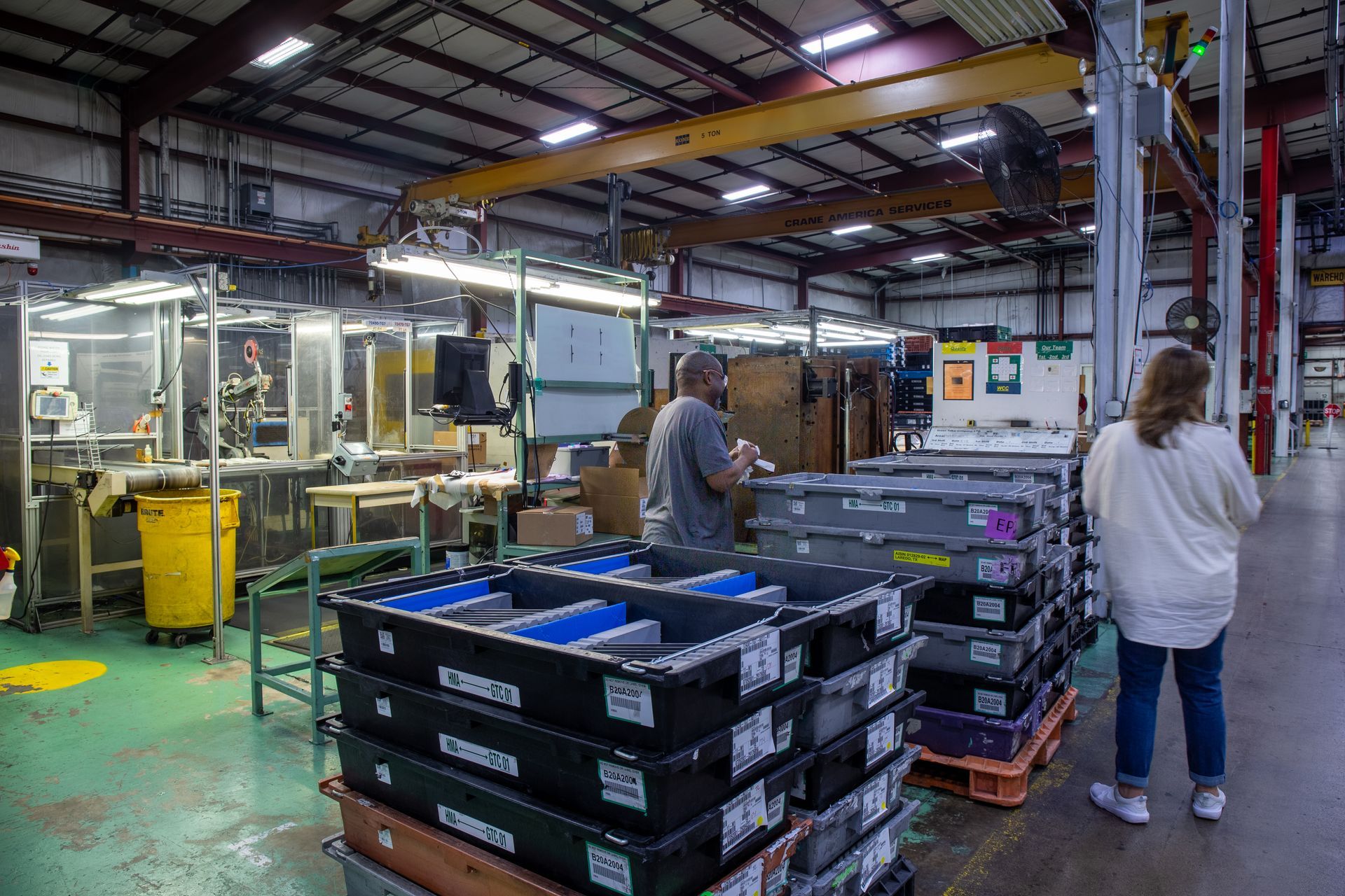 Factory interior with stacks of bins and two workers, one standing and one working.