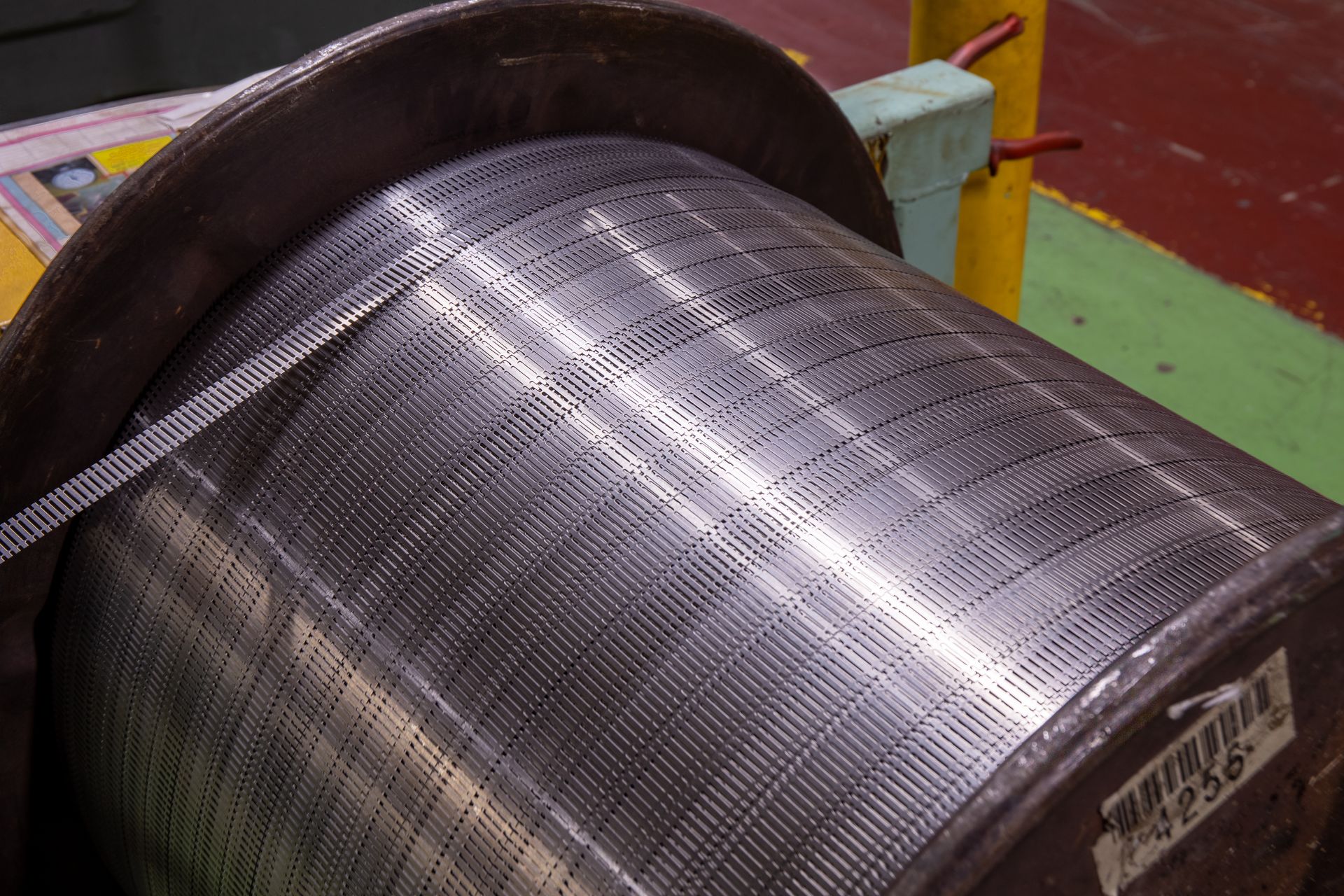 Spool of metallic, perforated ribbon wound on a large, cylindrical drum.