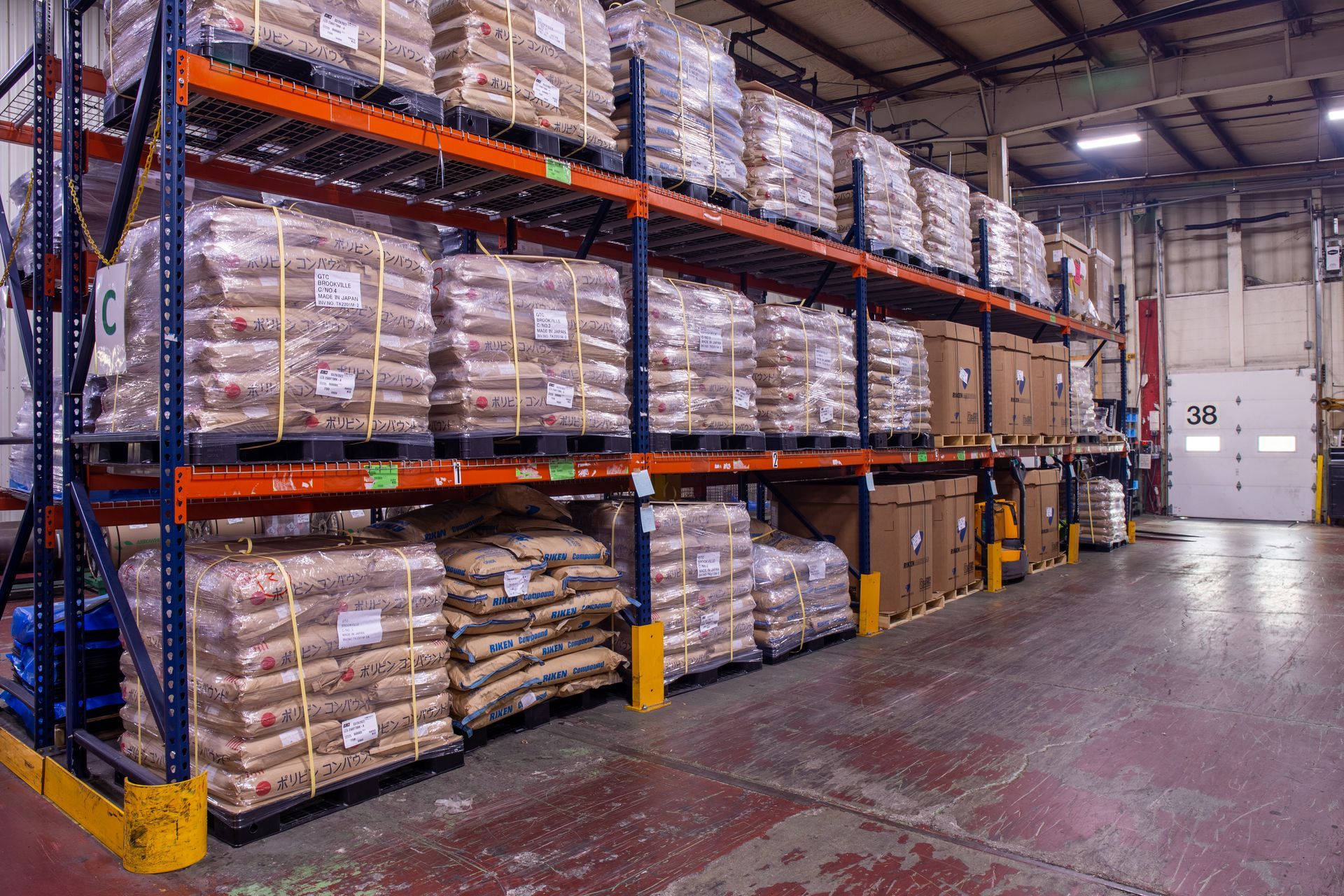 Warehouse interior: Shelves stacked with palletized bags and boxes. Orange, blue, and brown.