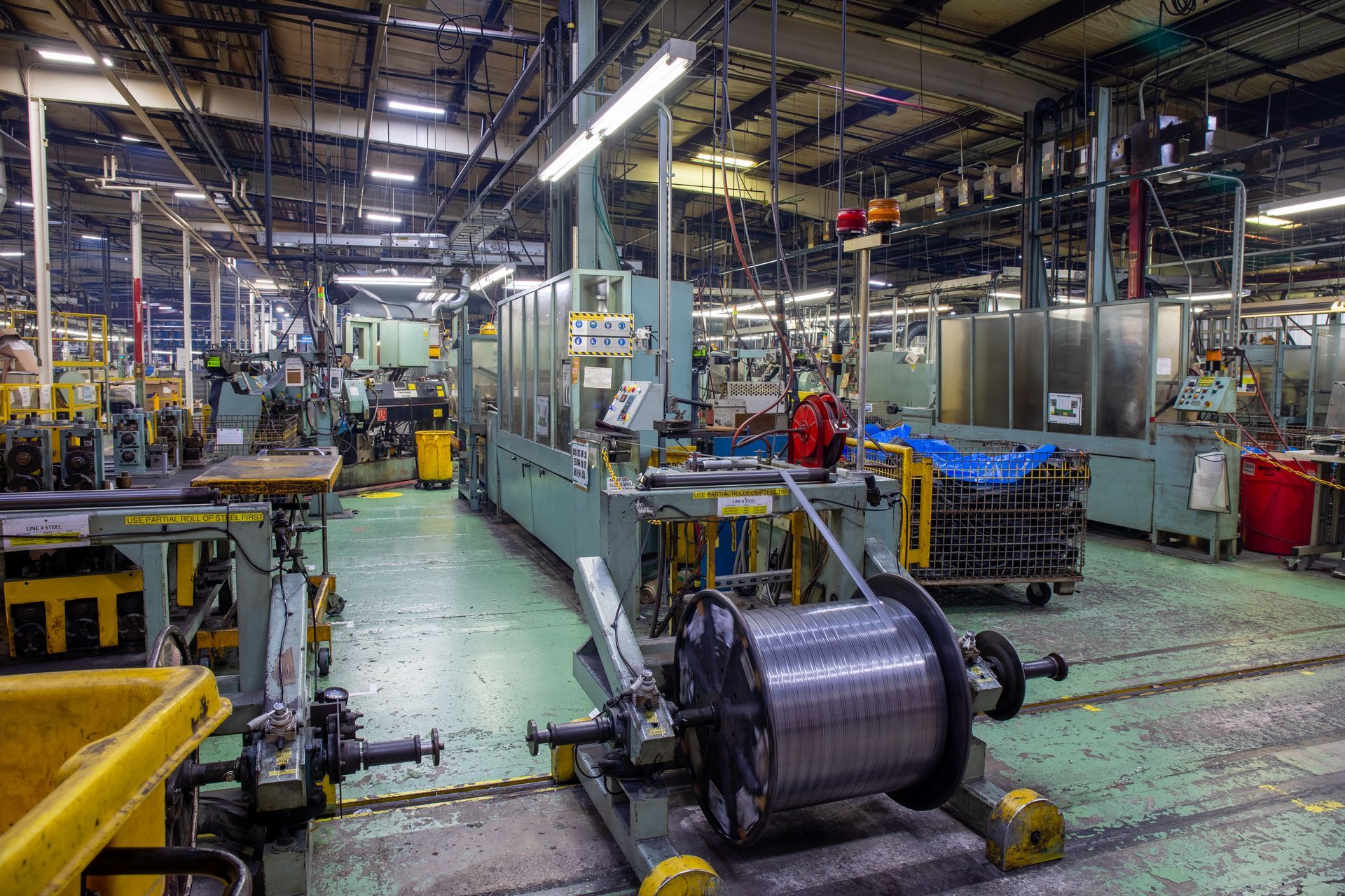 Factory floor with machinery and spools of metal wire. Industrial setting, equipment.