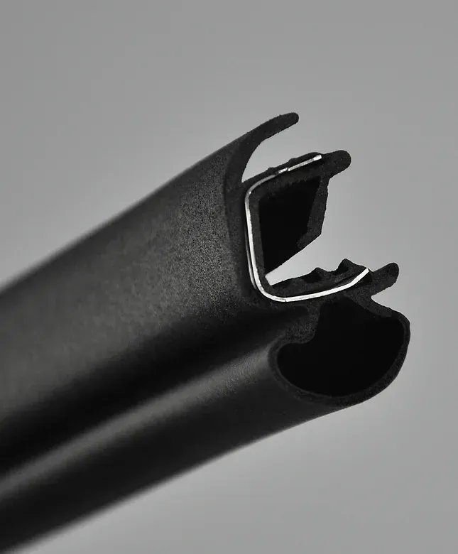 Black rubber weather stripping profile, close-up, showing a curved shape with a channel for gripping.