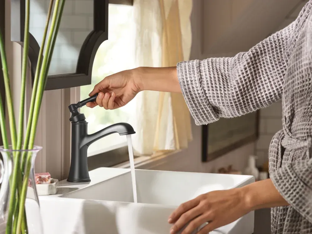 Person washing hands at a sink with a black faucet, water running into a white basin.